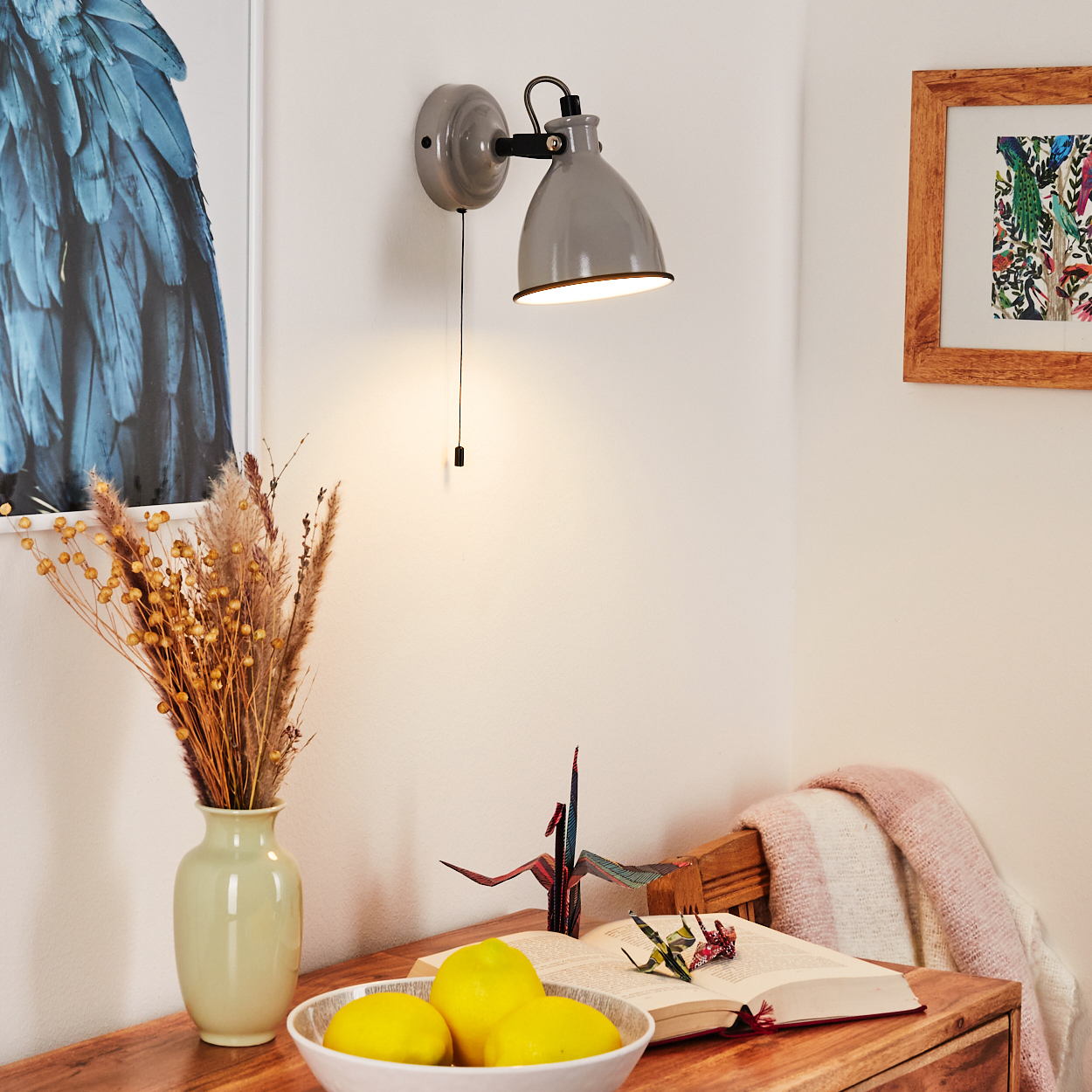 Graue Wandlampe über einem Tisch mit Vase, Zitronen und Buch.