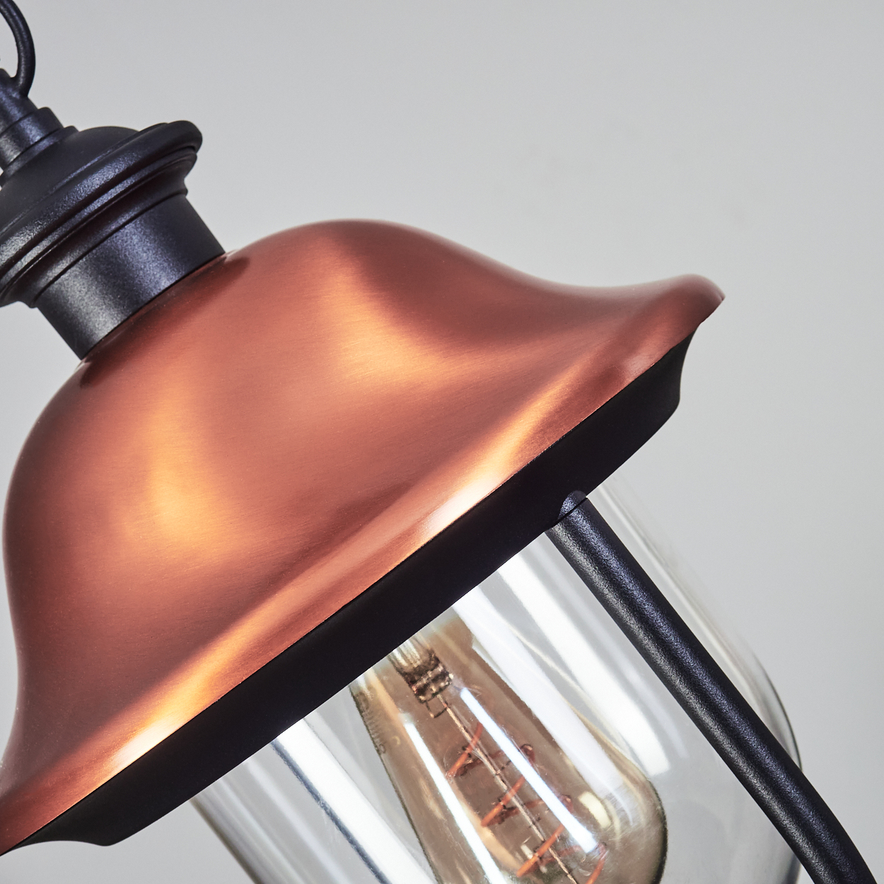 Eine kupferfarbene Lampe mit schwarzem Metall und Glas. Glühbirne sichtbar.