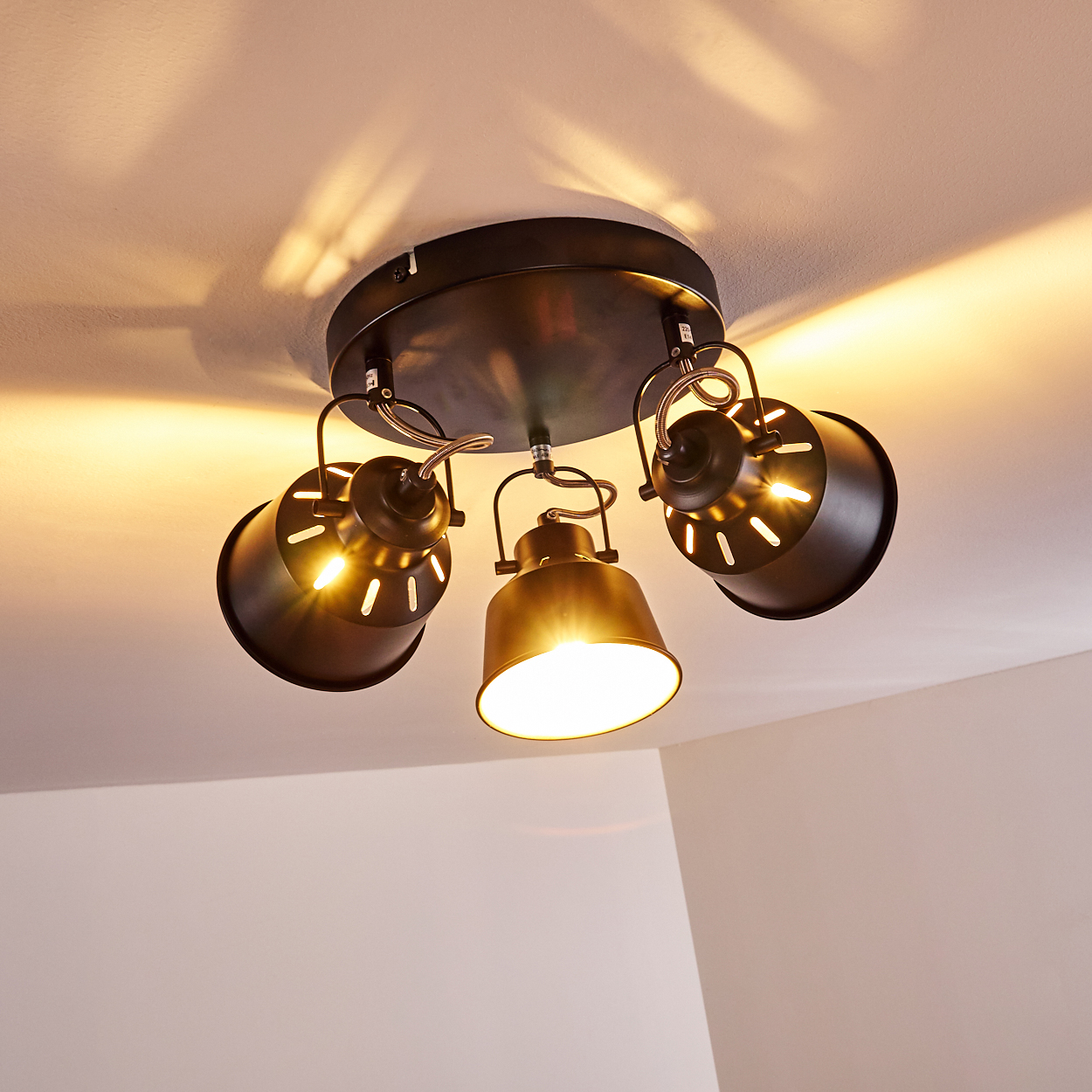 Deckenleuchte mit drei verstellbaren Spots in Dunkelbraun, die Licht auf die weiße Decke werfen.
