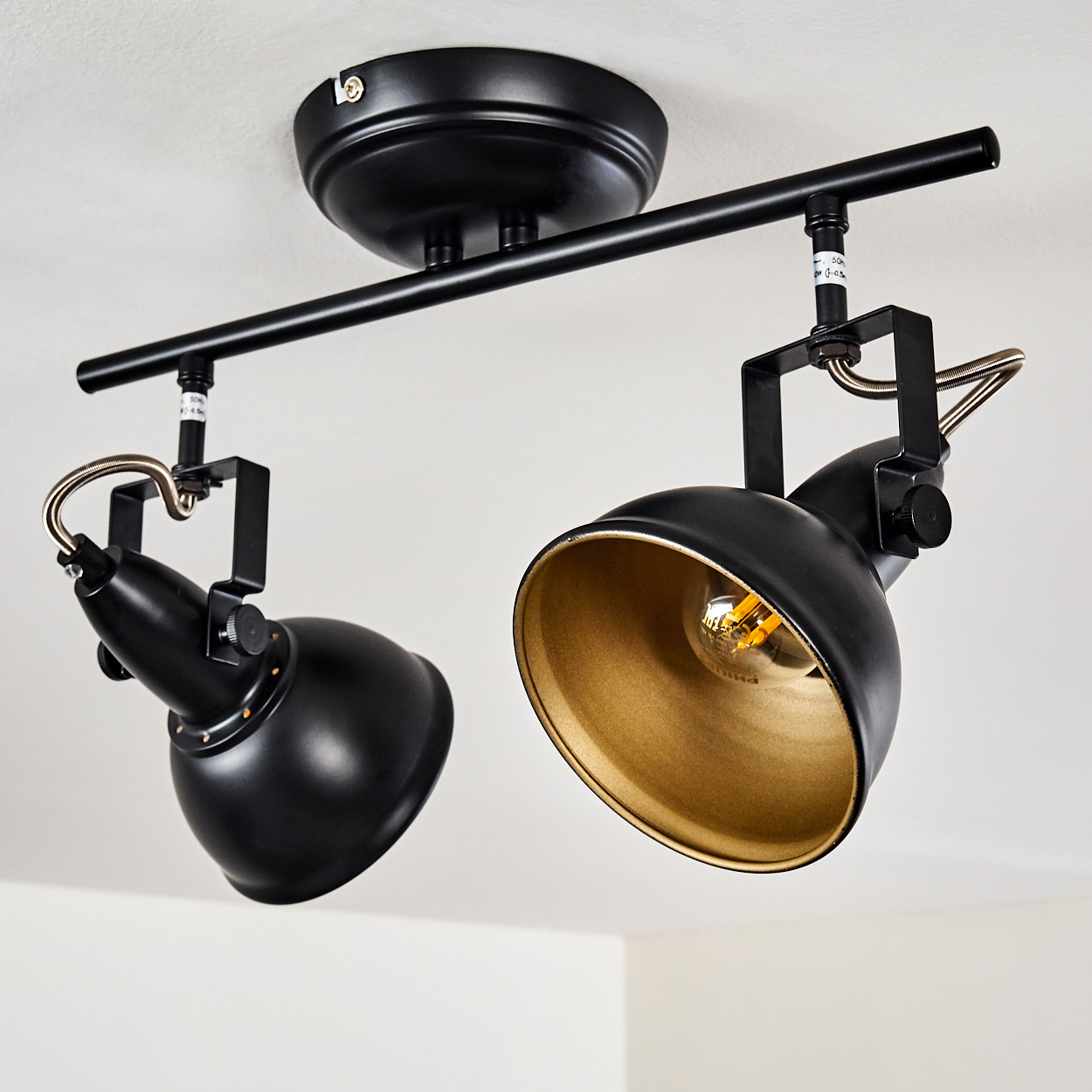 Zwei schwarze Schienenstrahler mit goldenen Innenseiten an einer Decke.