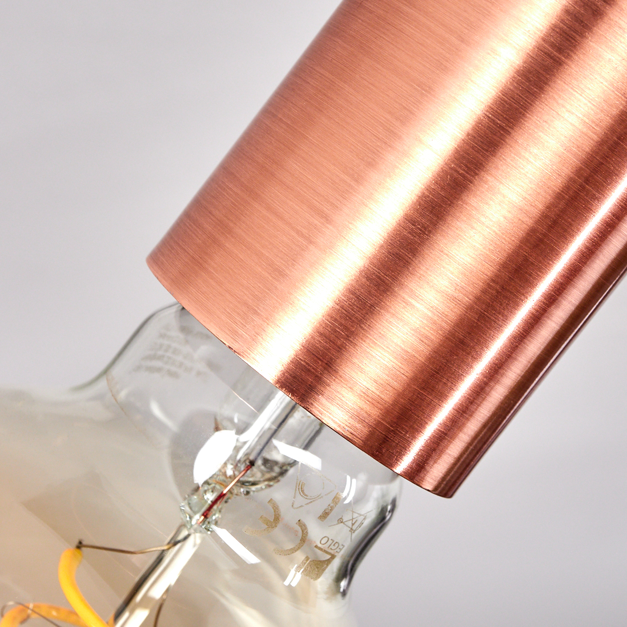 Nahaufnahme einer Kupferschirm-Lampe mit Glasbirne und sichtbaren Drähten.