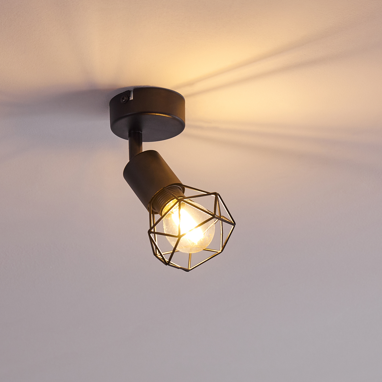 Schwarzer Deckenstrahler mit Käfig-Lampenschirm, der Licht abstrahlt.