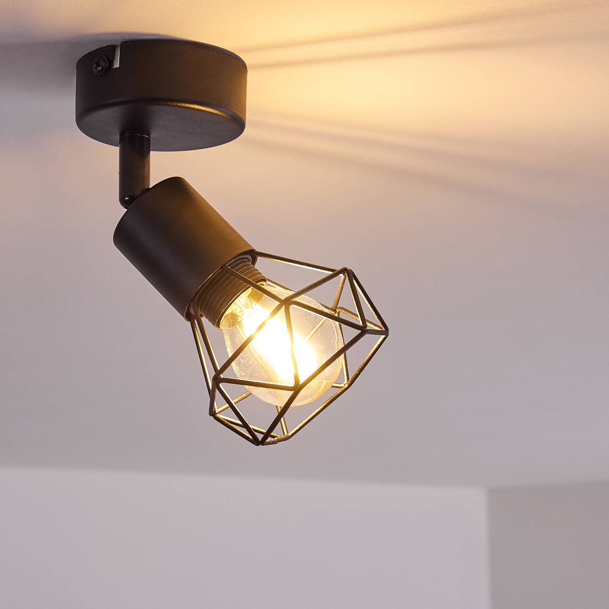 Schwarzer Deckenstrahler mit geometrischem Käfig und Glühbirne, der Licht ausstrahlt.