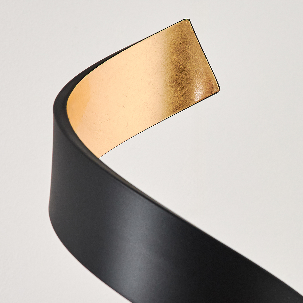 Ein schwarzes Band biegt sich mit einer goldenen Innenseite vor einem weißen Hintergrund.