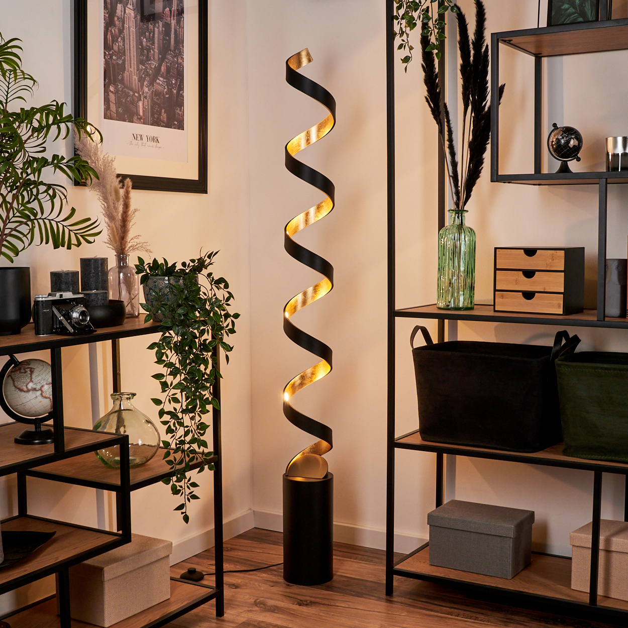 Eine moderne schwarze Stehlampe mit goldener Spirale steht neben einem Regal mit Pflanzen.