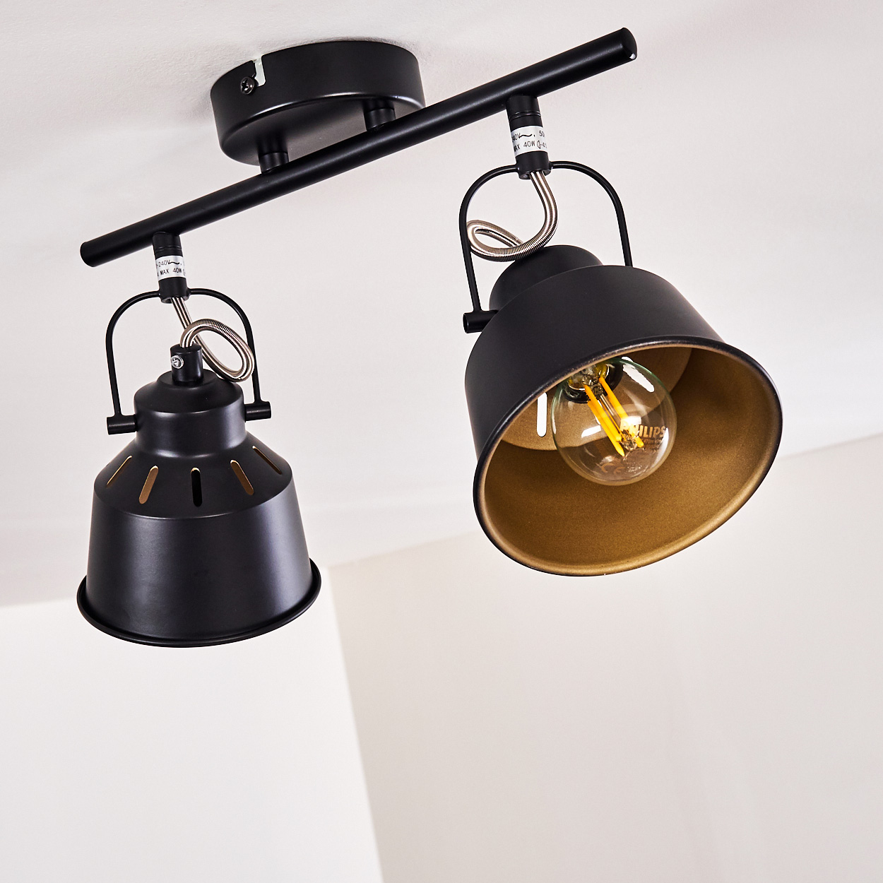 Zwei schwarze Deckenstrahler mit goldenen Innenseiten an einer Schiene.