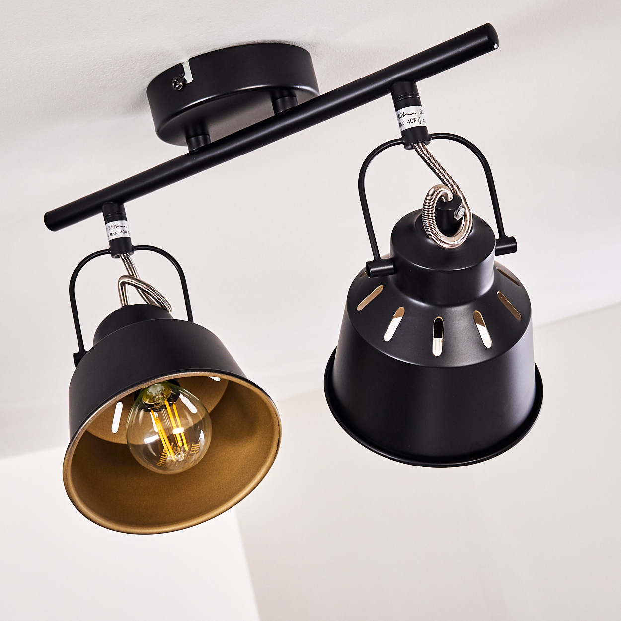 Zwei schwarze Lampenschirme mit goldener Innenseite hängen an einer Stange.