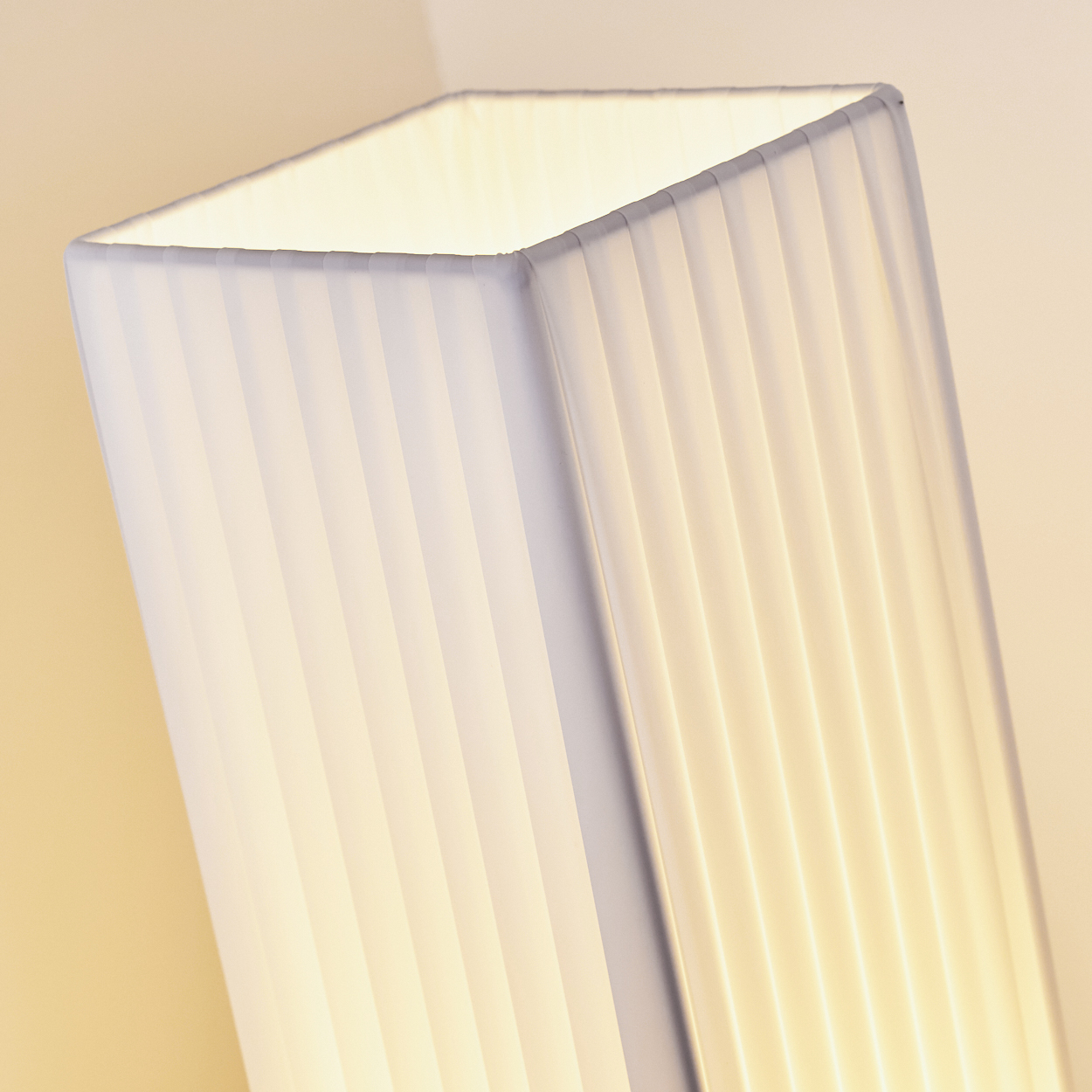 Eine weiße, gefaltete Lampe mit einem rechteckigen oberen Rand leuchtet warm.
