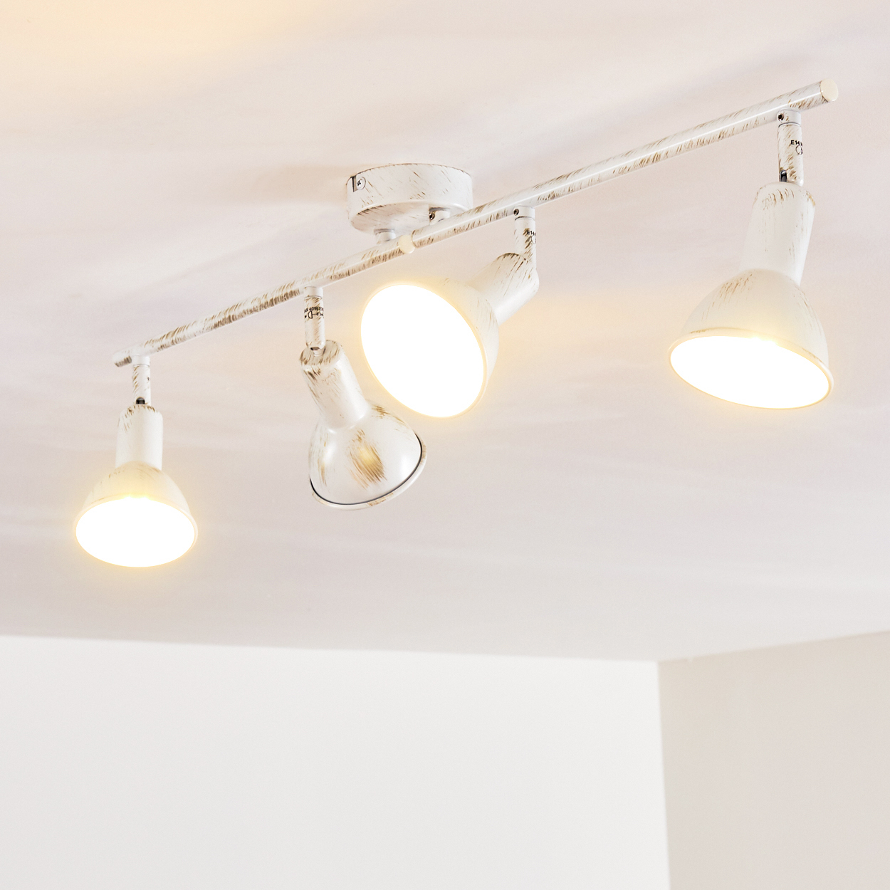 Eine weiße Vierer-Schienenleuchte mit distressed Finish an einer weißen Decke.