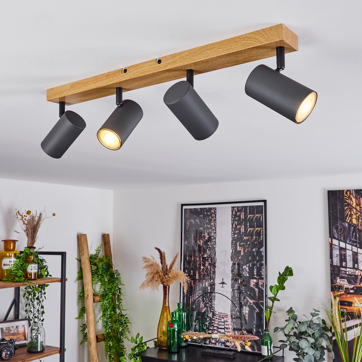 Eine Holzleiste mit vier schwarzen, schwenkbaren Spots, die an einer Decke montiert sind.