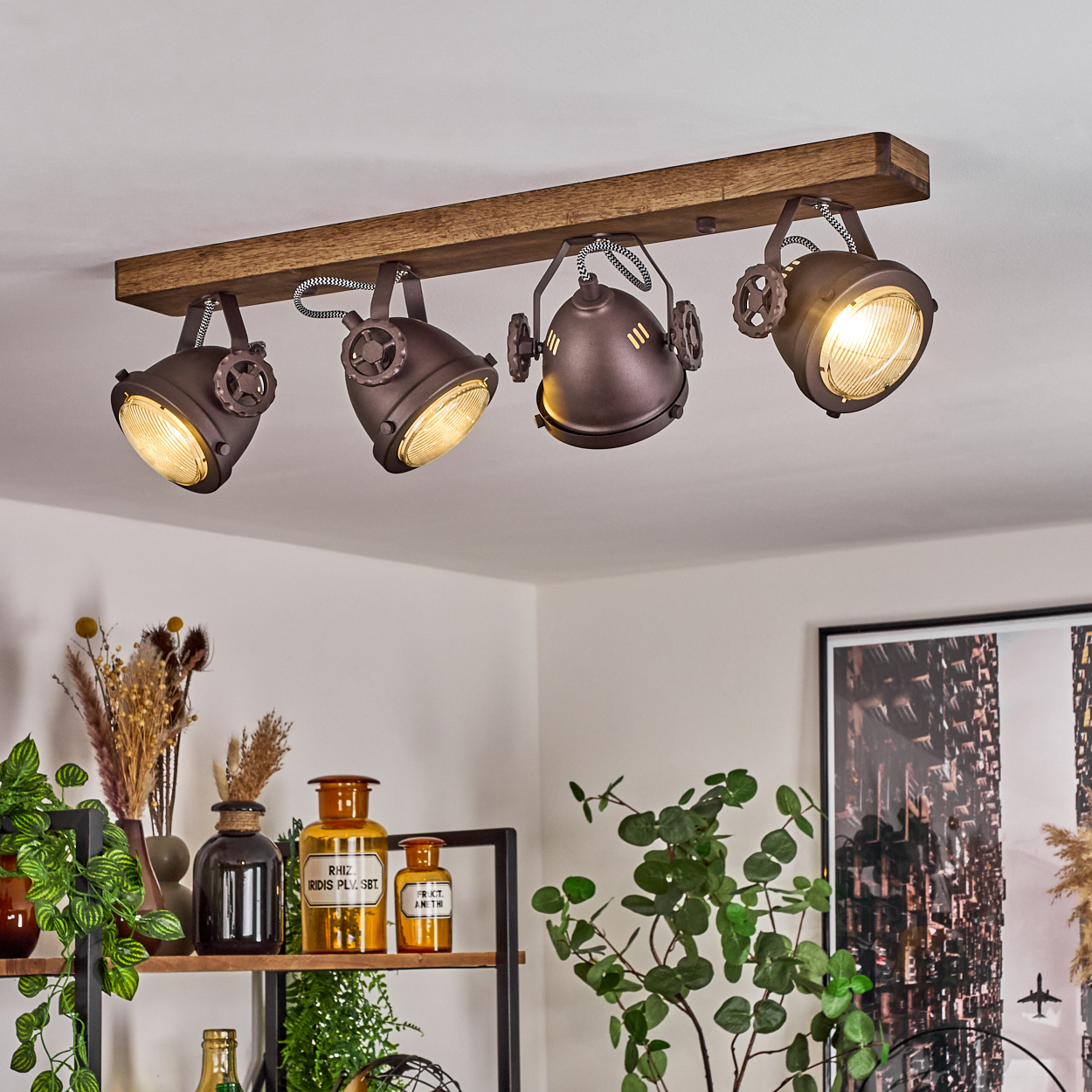 Ein Holzbalken trägt vier Spots im Industriestil, die einen Raum mit Pflanzen und Deko beleuchten.