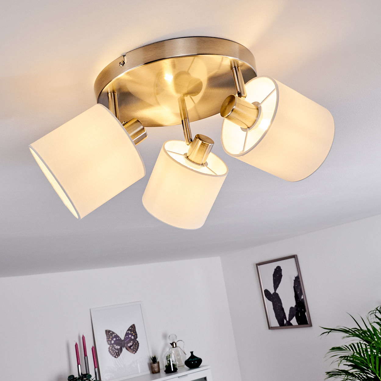 Deckenleuchte mit drei weißen Schirmen und Metallfassung an der Decke.