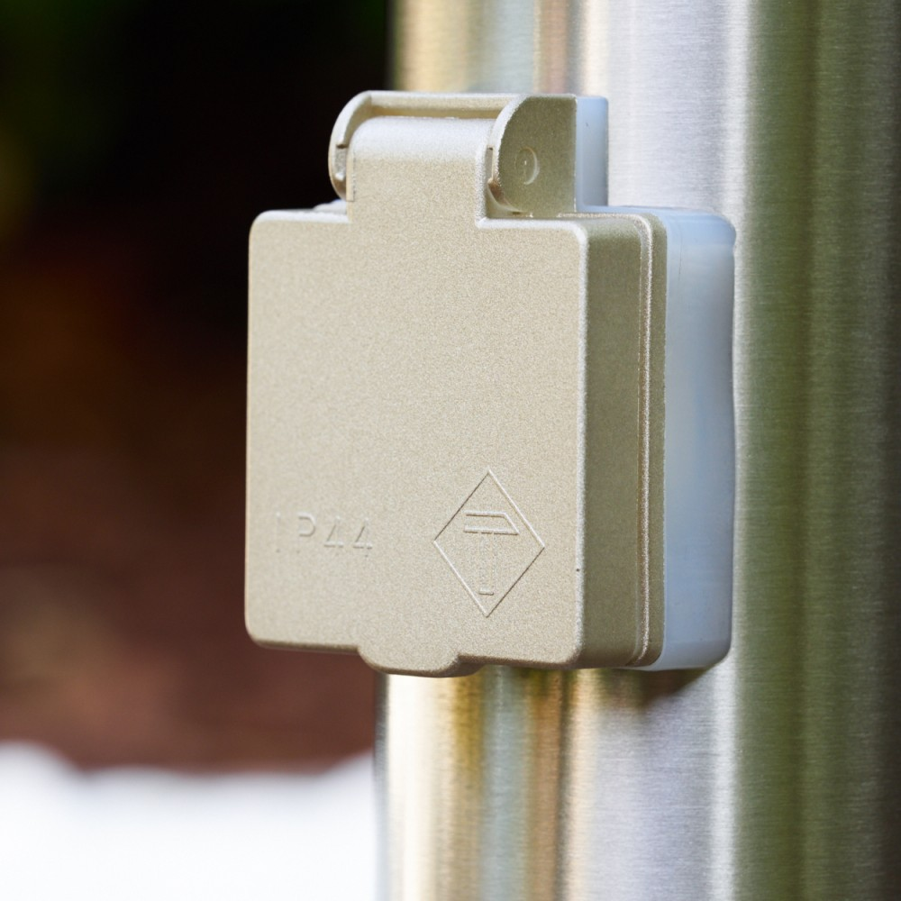 Eine beige Steckdose mit IP44-Kennzeichnung an einem Metallpfosten.