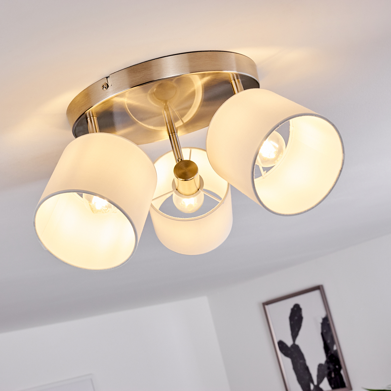 Deckenleuchte mit drei weißen Lampenschirmen und Messingdetails auf weißer Decke.