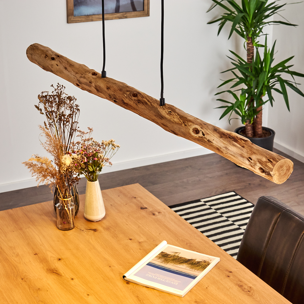 Ein rustikaler Baumstamm-Kronleuchter über einem Holztisch mit Vasen und Buch.