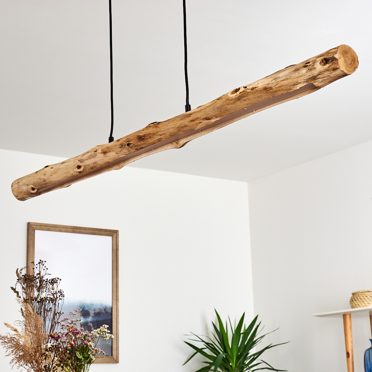 Ein rustikaler Holz-Pendelleuchter hängt von der Decke über einem Tisch mit Trockenblumen.