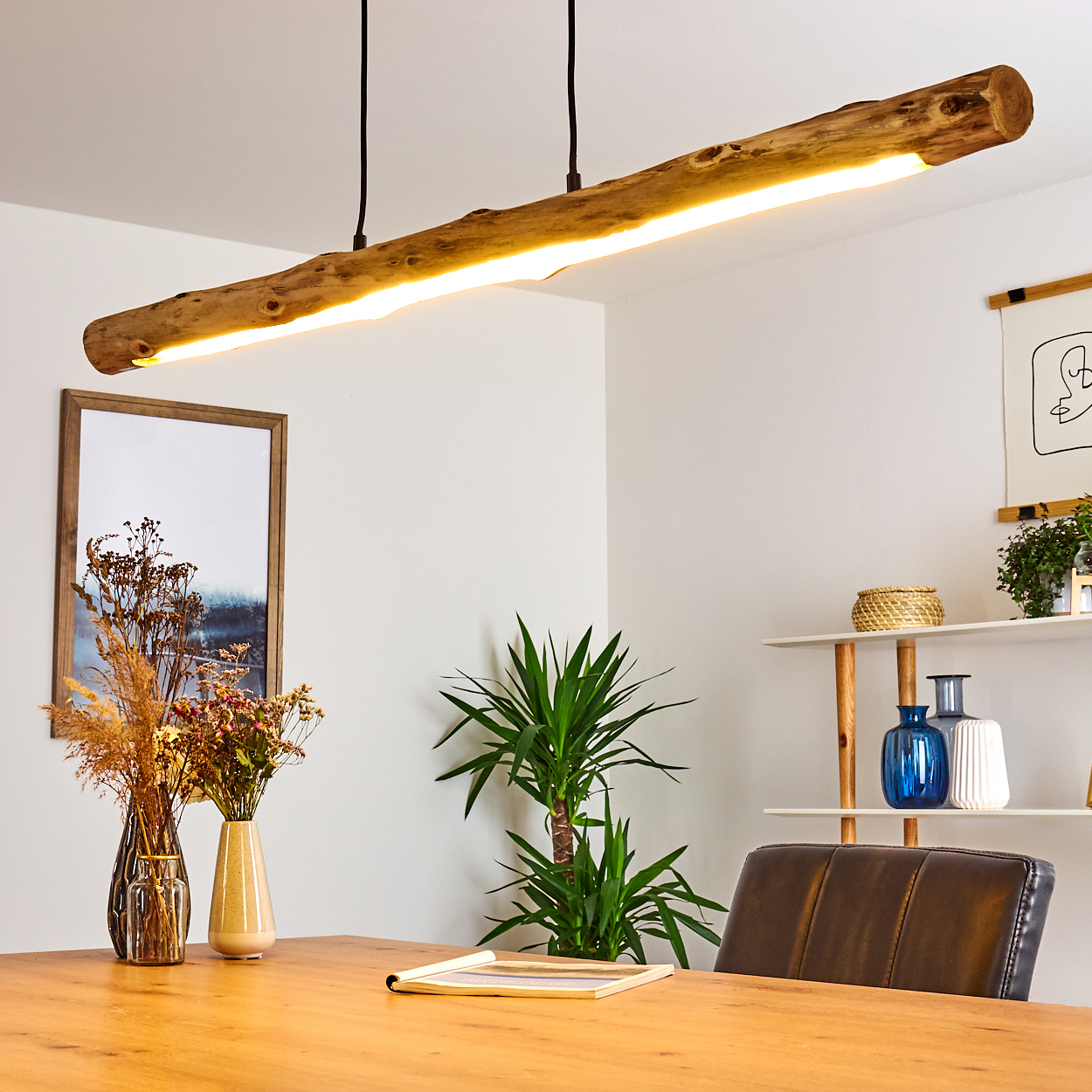 Eine rustikale Holzlampe hängt über einem Esstisch mit Vasen und Pflanzen.