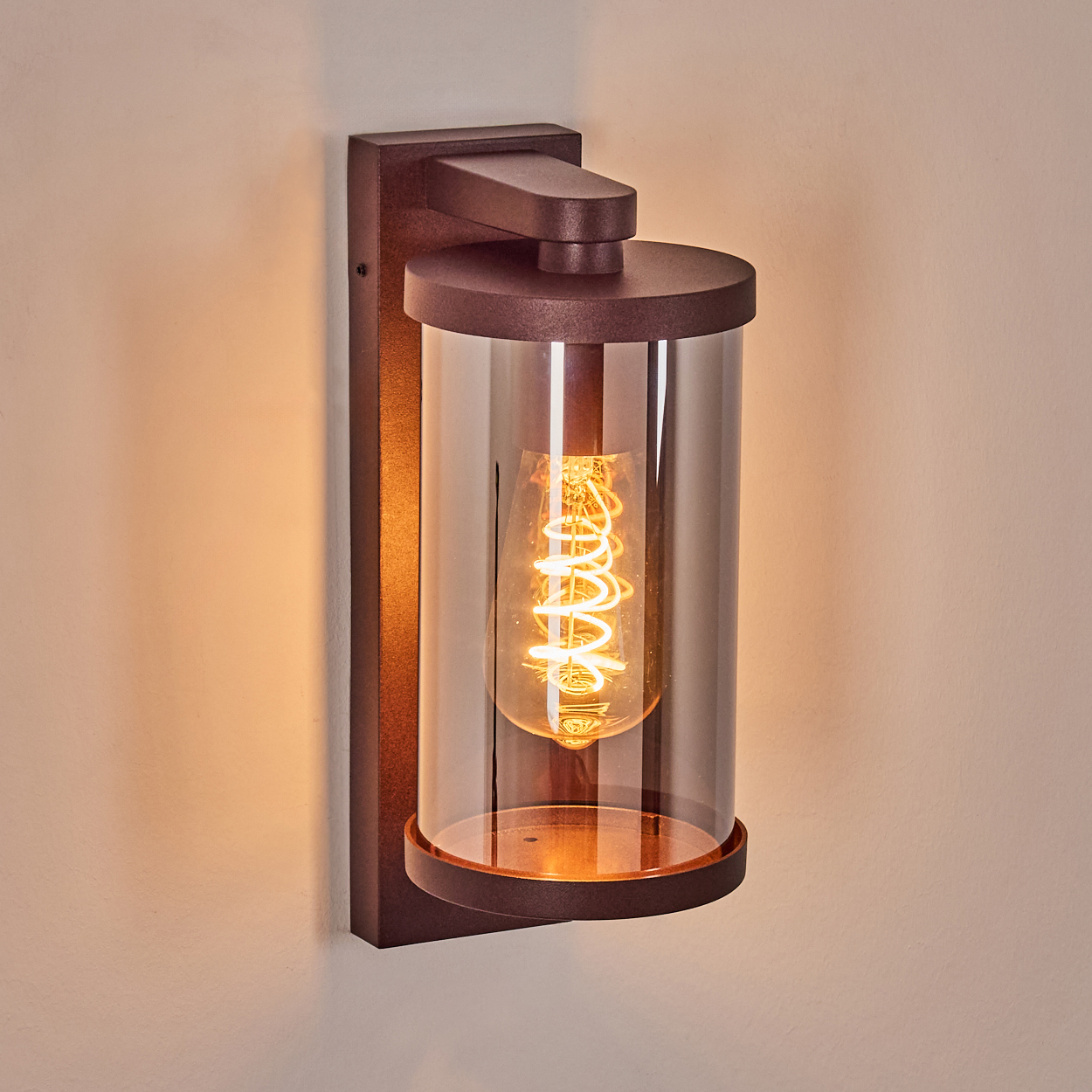 Eine braune Wandleuchte mit zylindrischem Glas und Edison-Glühbirne.