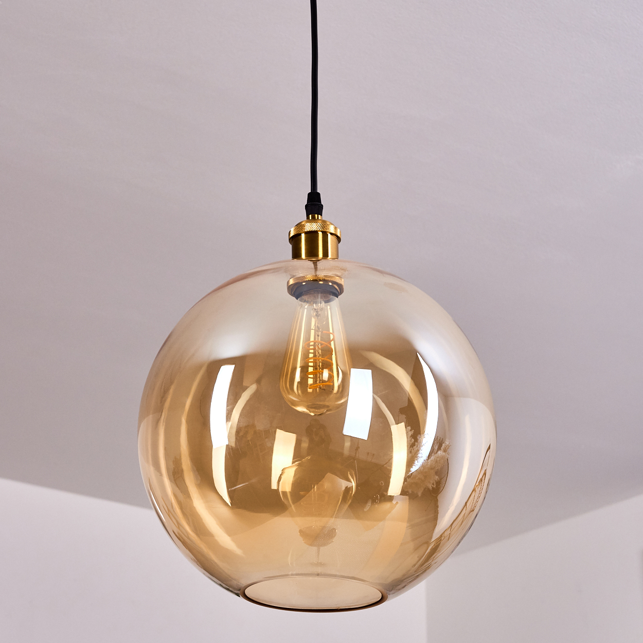 Eine bernsteinfarbene Glaspendelleuchte mit einem sichtbaren Edison-Glühbirnen-Stil-Leuchtmittel.