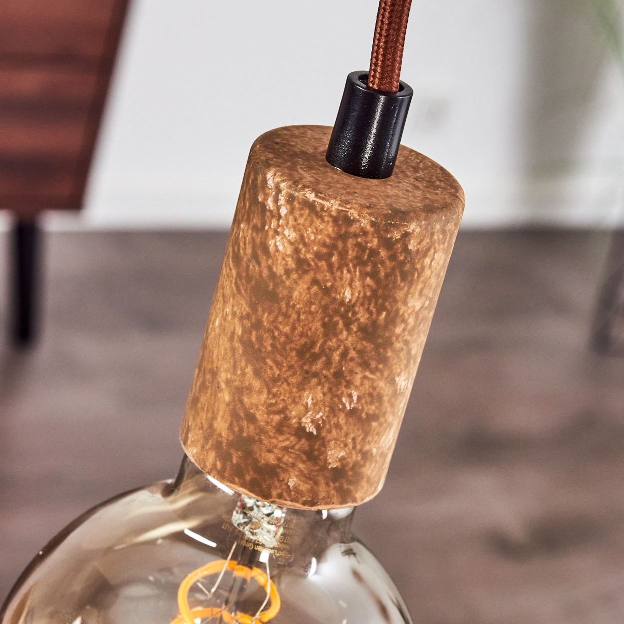 Eine kupferfarbene Lampenfassung mit braunem Kabel und Glühbirne.