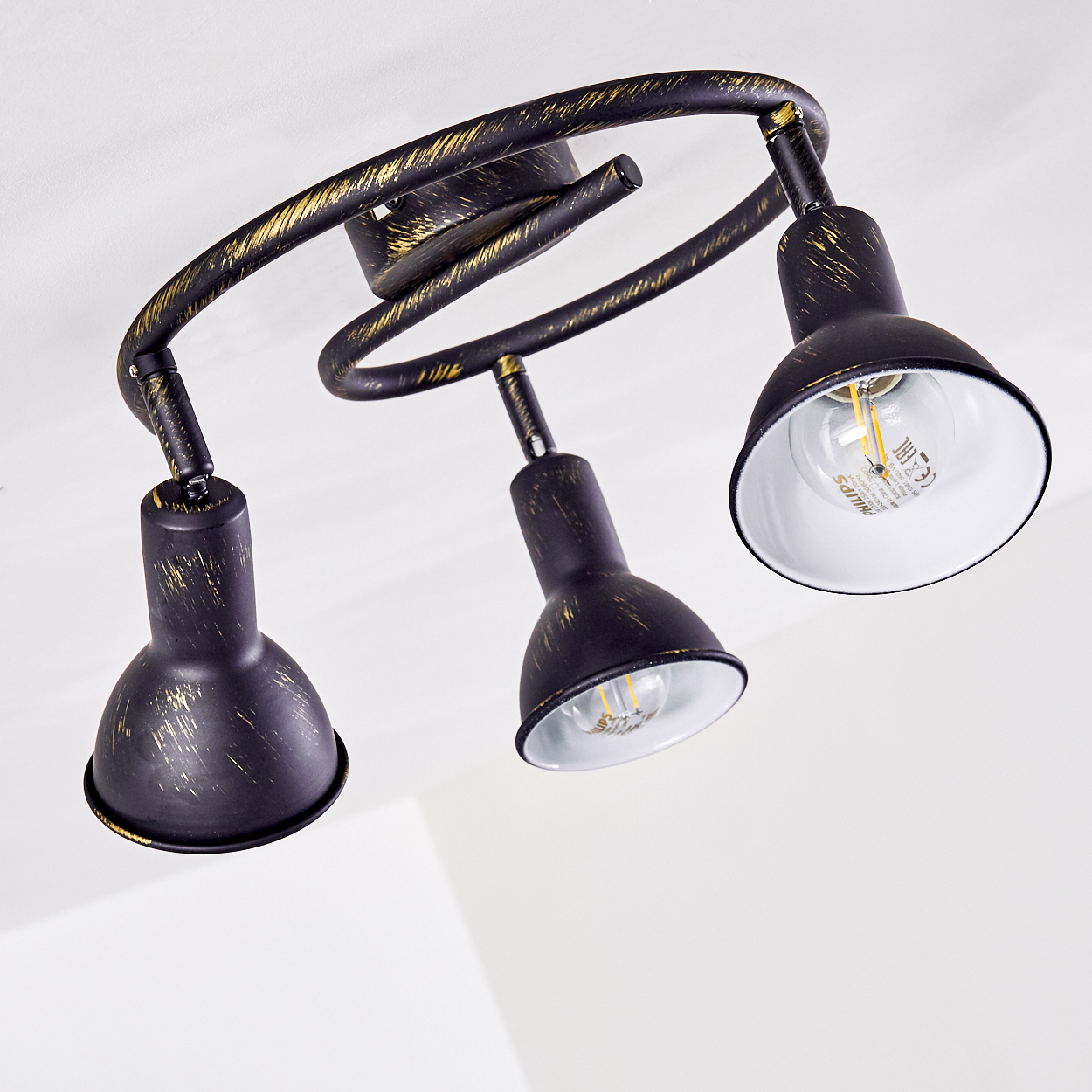 Schwarze Lampe mit Goldakzenten und drei verstellbaren Lampenschirmen an einer geschwungenen Leiste.