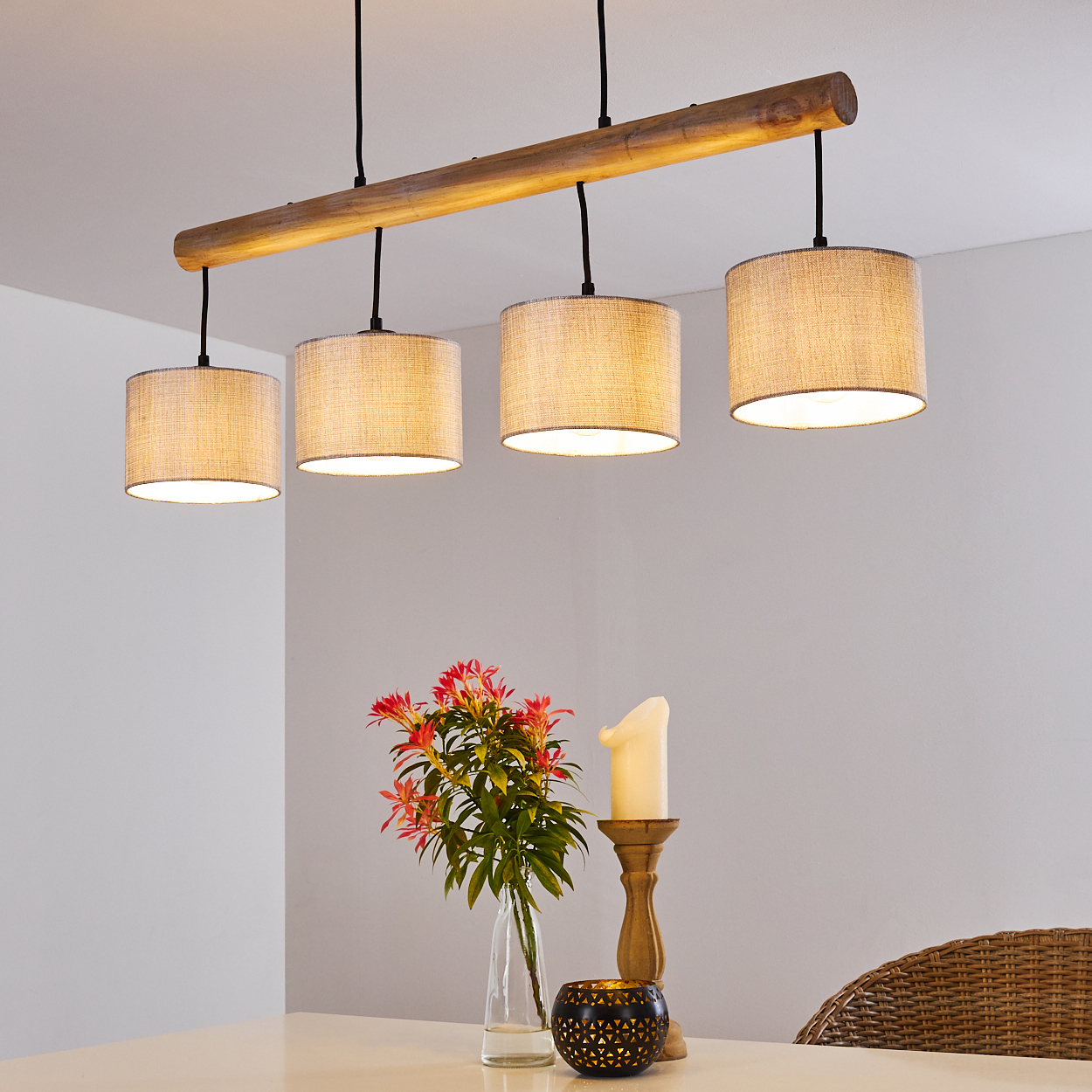 Ein Lampen-Kronleuchter mit vier Lampenschirmen hängt über einem Tisch mit Blumen und Kerzen.