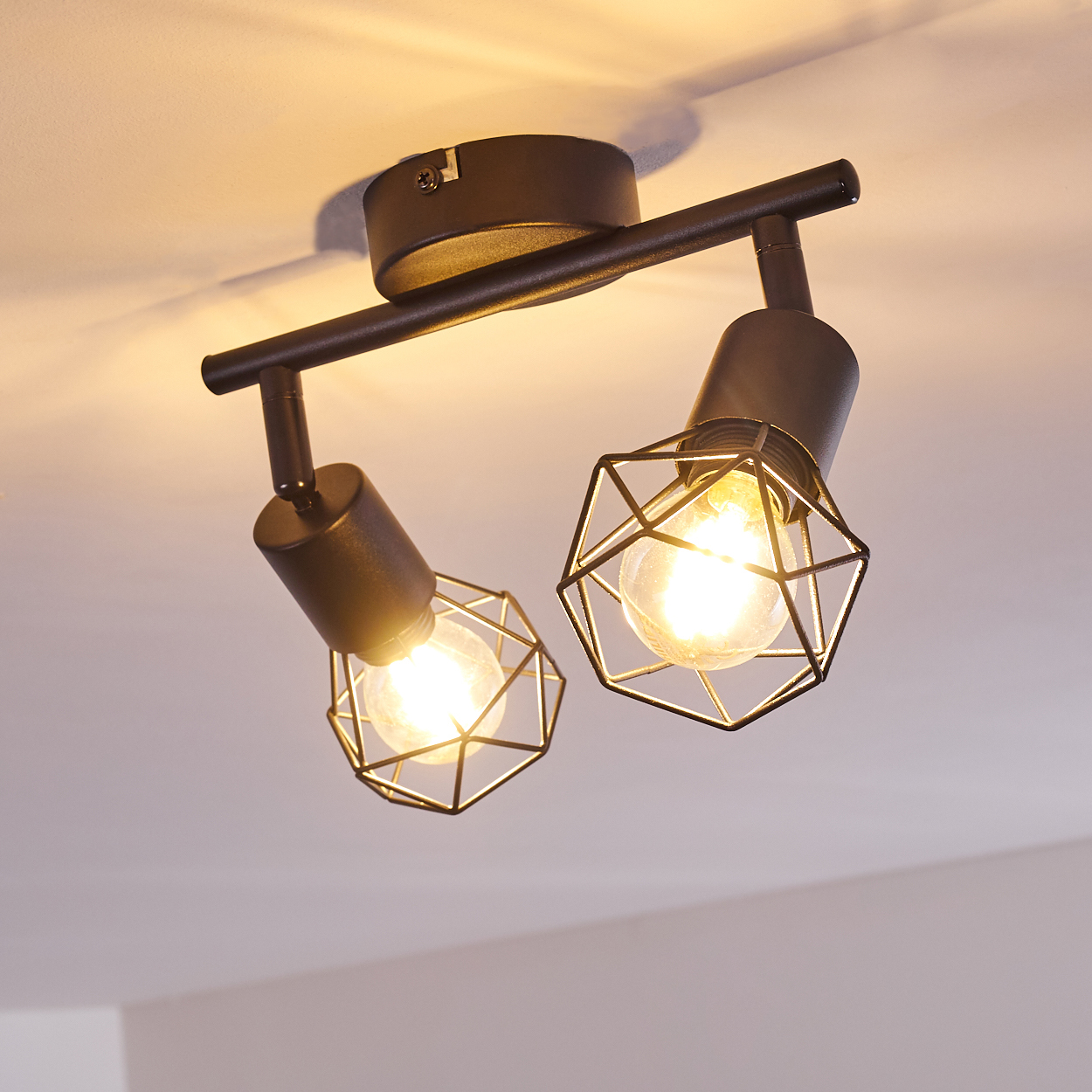 Dunkler Deckenstrahler mit zwei Lampen und geometrischen Käfigschirmen.