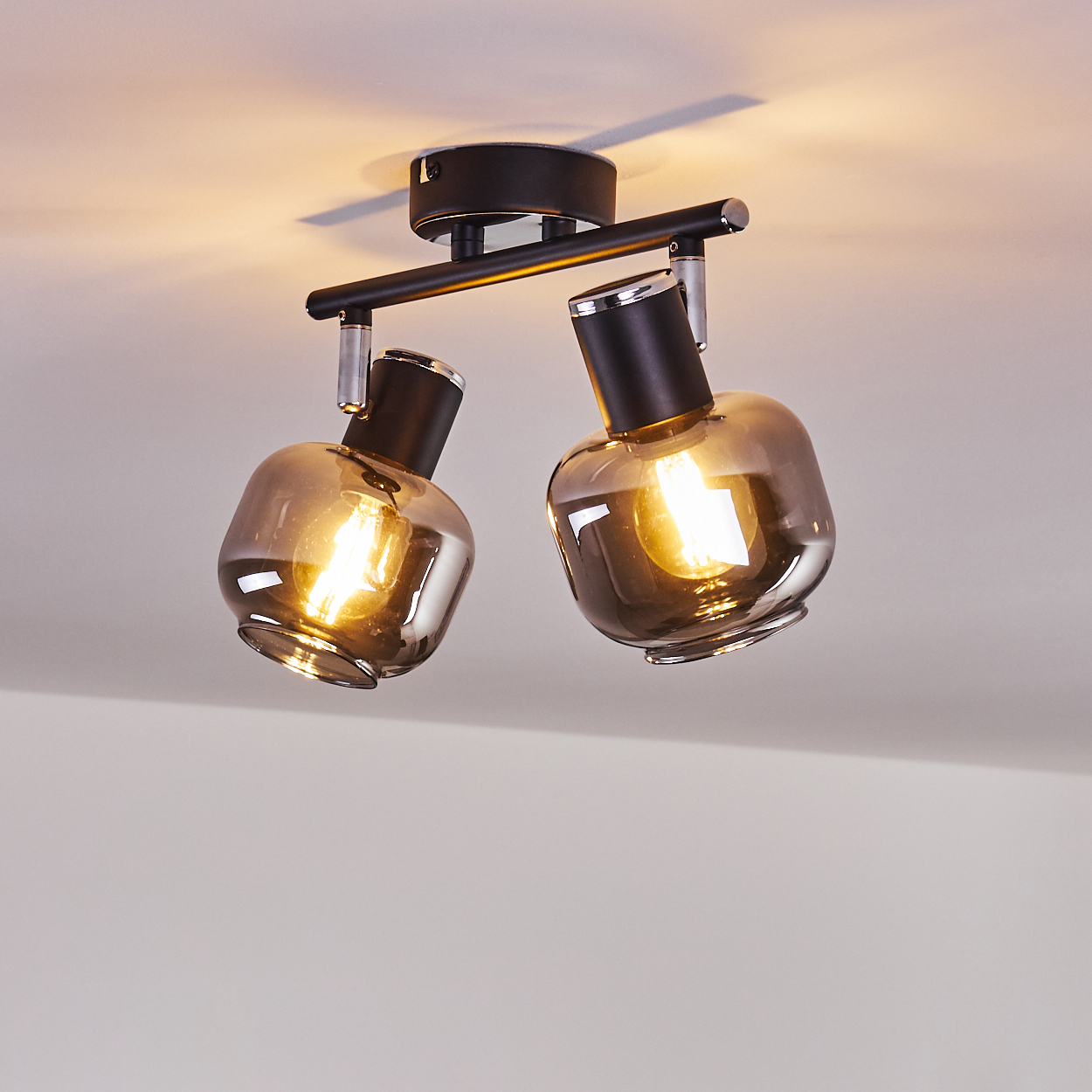 Zwei rauchglas Lampen mit sichtbaren Glühbirnen an einer schwarzen Deckenleuchte.