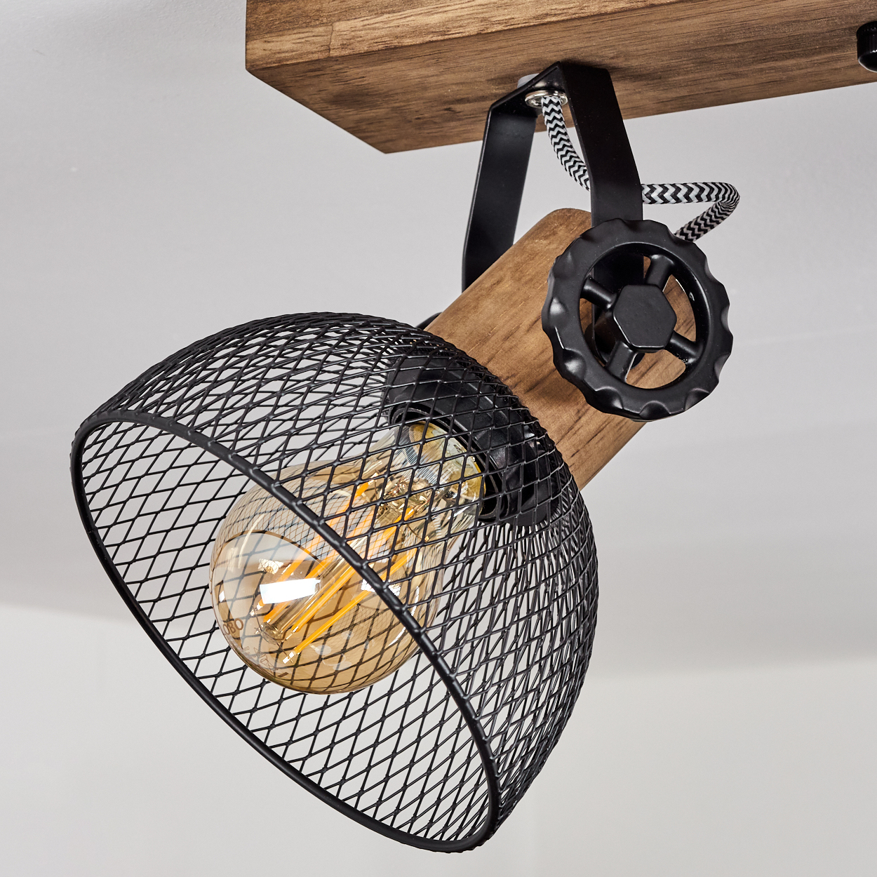 Industrielle Lampe mit Holzbalken, schwarzem Drahtkorb und Glühbirne.