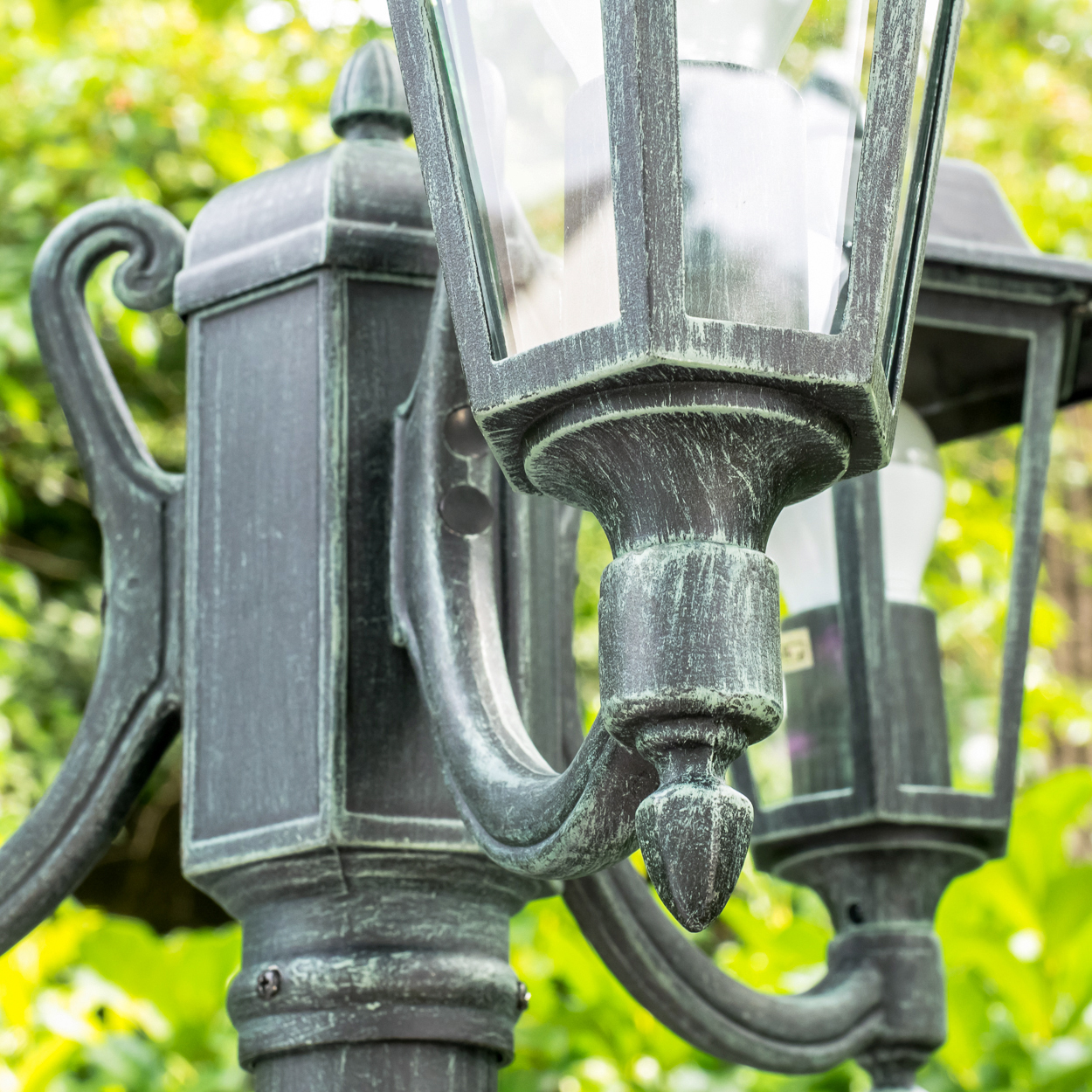 Eine dunkle Laterne mit Glas, im Grünen, mit Verzierungen.