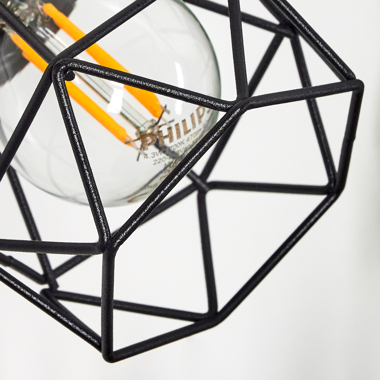 Eine schwarze geometrische Lampe mit einem sichtbaren Glühfaden und orangefarbenen Elementen.