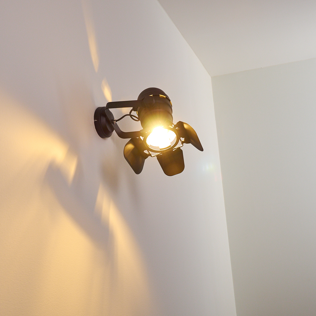 Ein dunkler Scheinwerfer an einer weißen Wand wirft gelbes Licht und Schatten.
