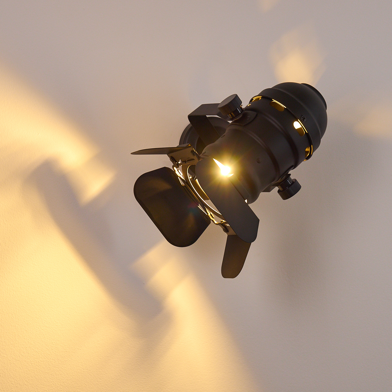 Ein schwarzer Scheinwerfer mit verstellbaren Flügeln leuchtet auf eine weiße Wand.