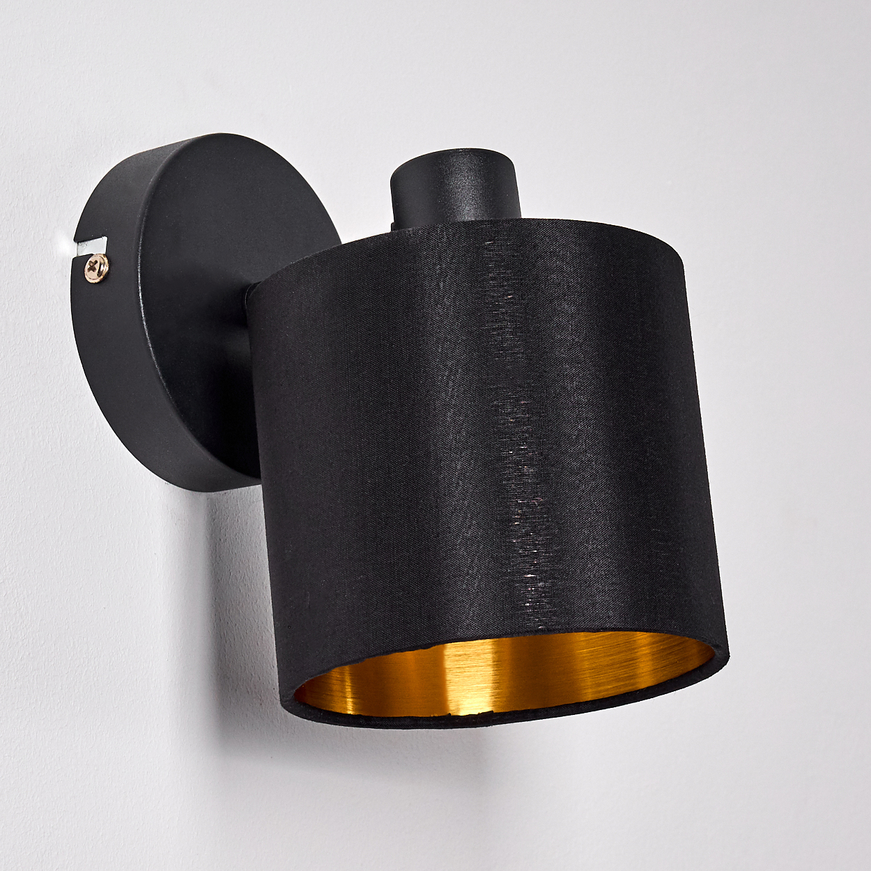 Schwarze Wandleuchte mit goldenem Innenschirm, montiert an einer weißen Wand.