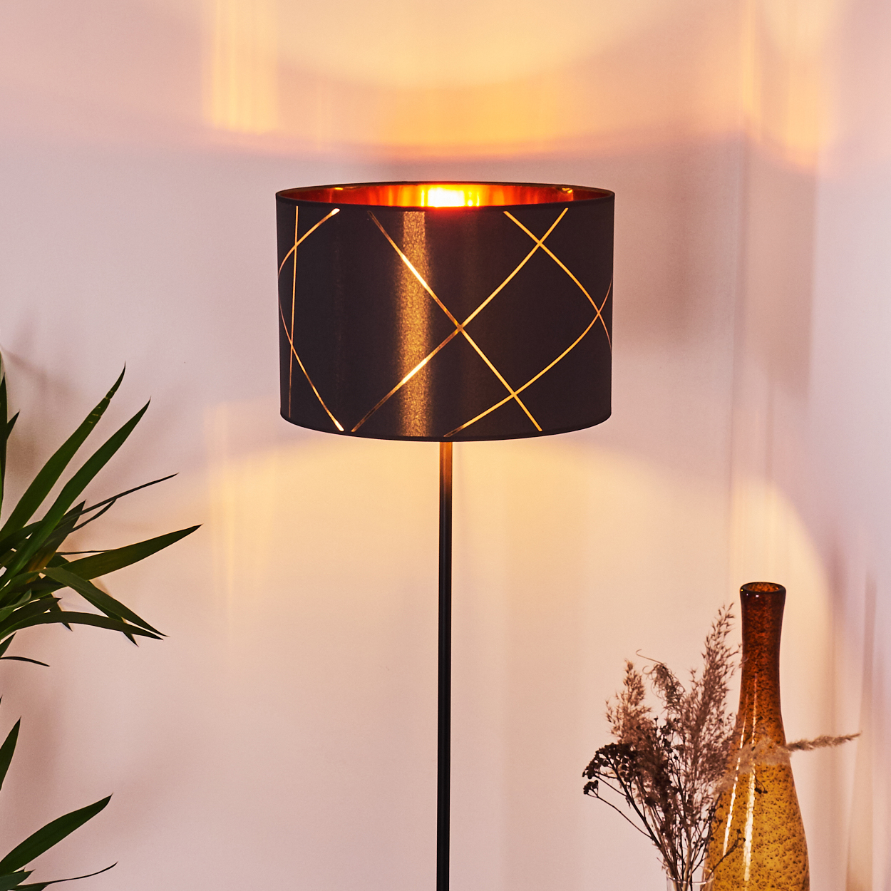Ein moderner schwarzer Stehleuchte mit goldenem Muster und warmem Licht.