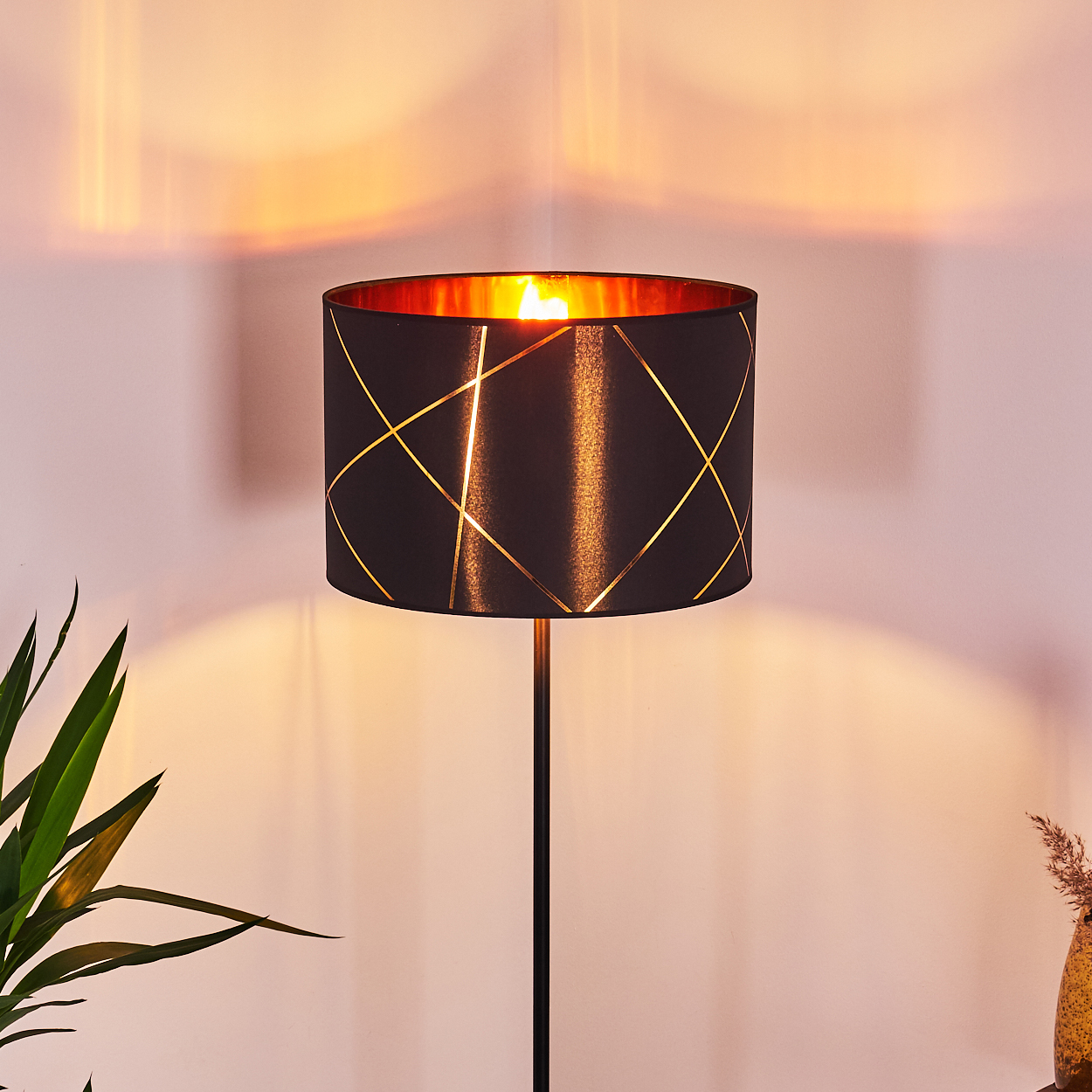 Schwarzer Lampenschirm mit goldenen Linien, beleuchtet von innen.