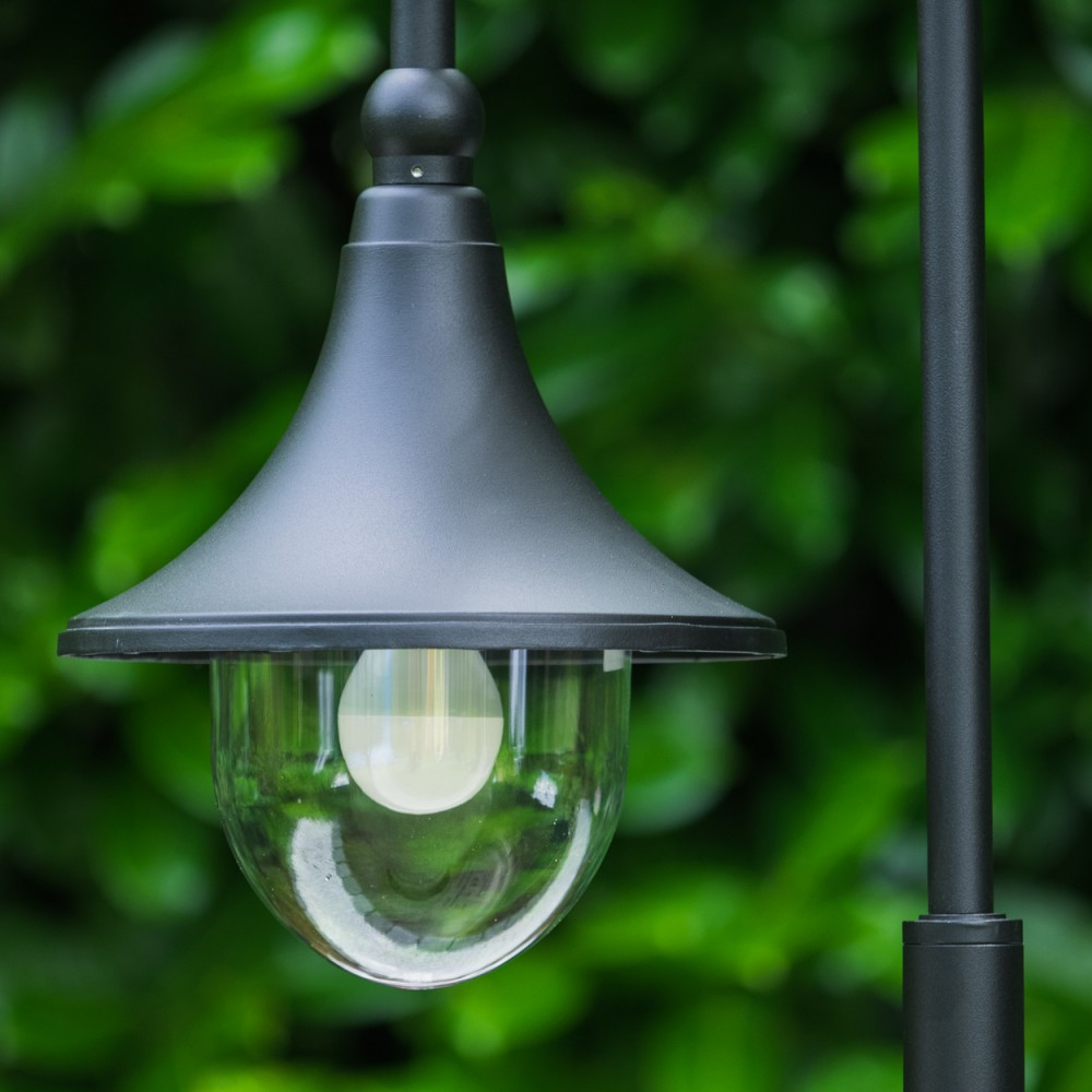 Eine schwarze Lampe mit Glaskuppel vor grünem Blätterhintergrund.