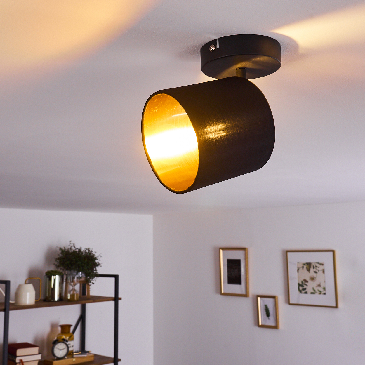 Schwarzer Deckenstrahler mit goldenem Innenteil leuchtet auf weißer Decke.