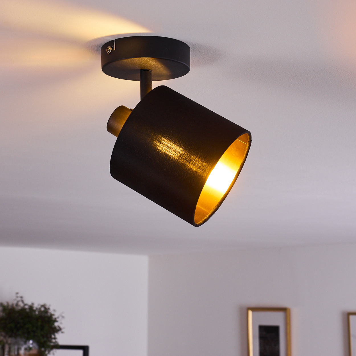Ein schwarzer Deckenstrahler mit goldenem Inneren leuchtet warm.