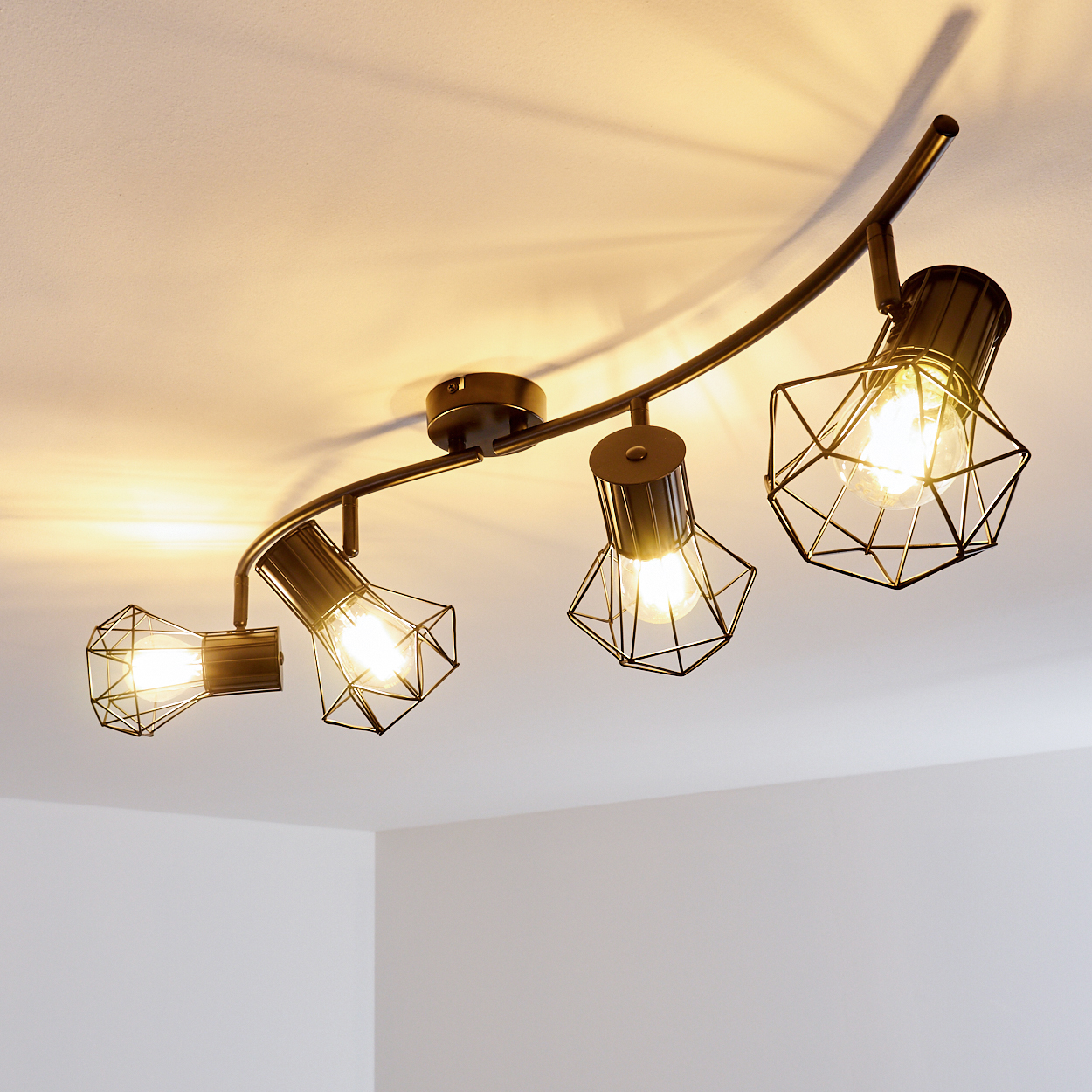 Schwarzer Deckenstrahler mit vier geometrischen Lampenschirmen und sichtbaren Glühbirnen.