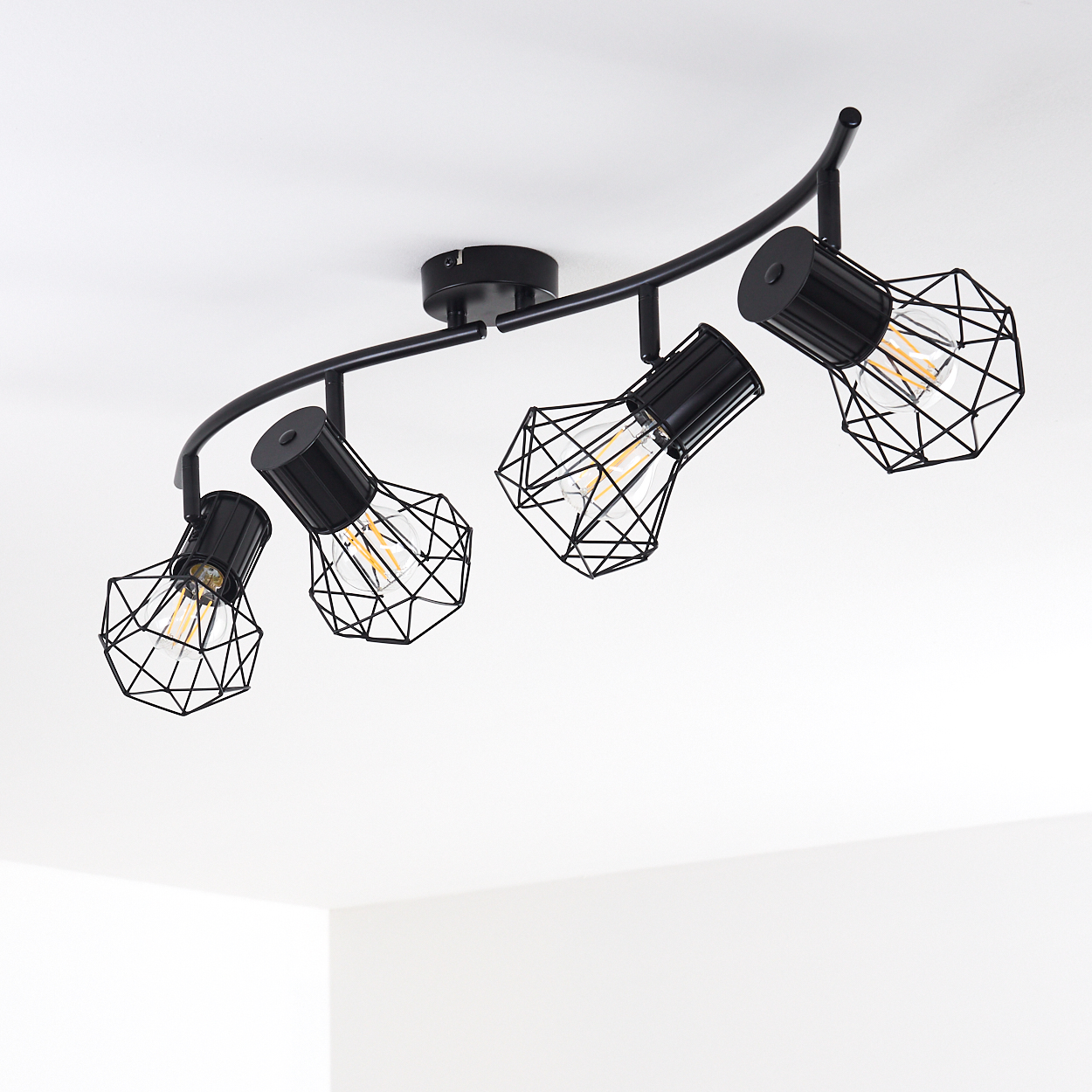 Eine schwarze gebogene Schienenleuchte mit vier Edison-Glühbirnen und geometrischen Käfigen.