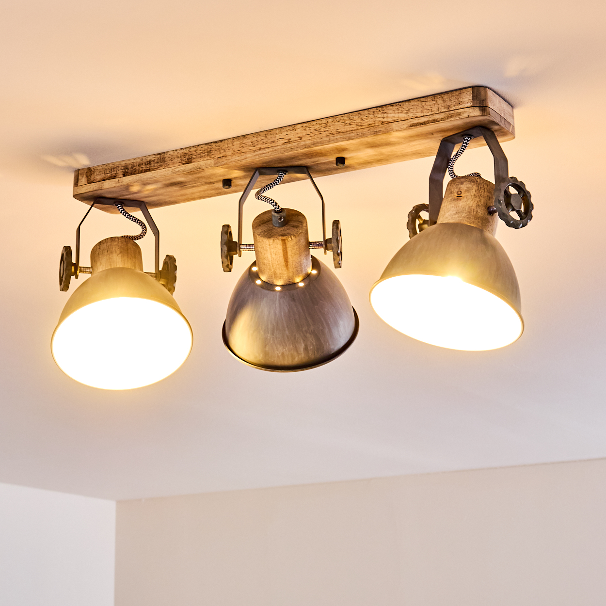 Deckenleuchte mit Holzsockel und drei verstellbaren Metalllampenschirmen.