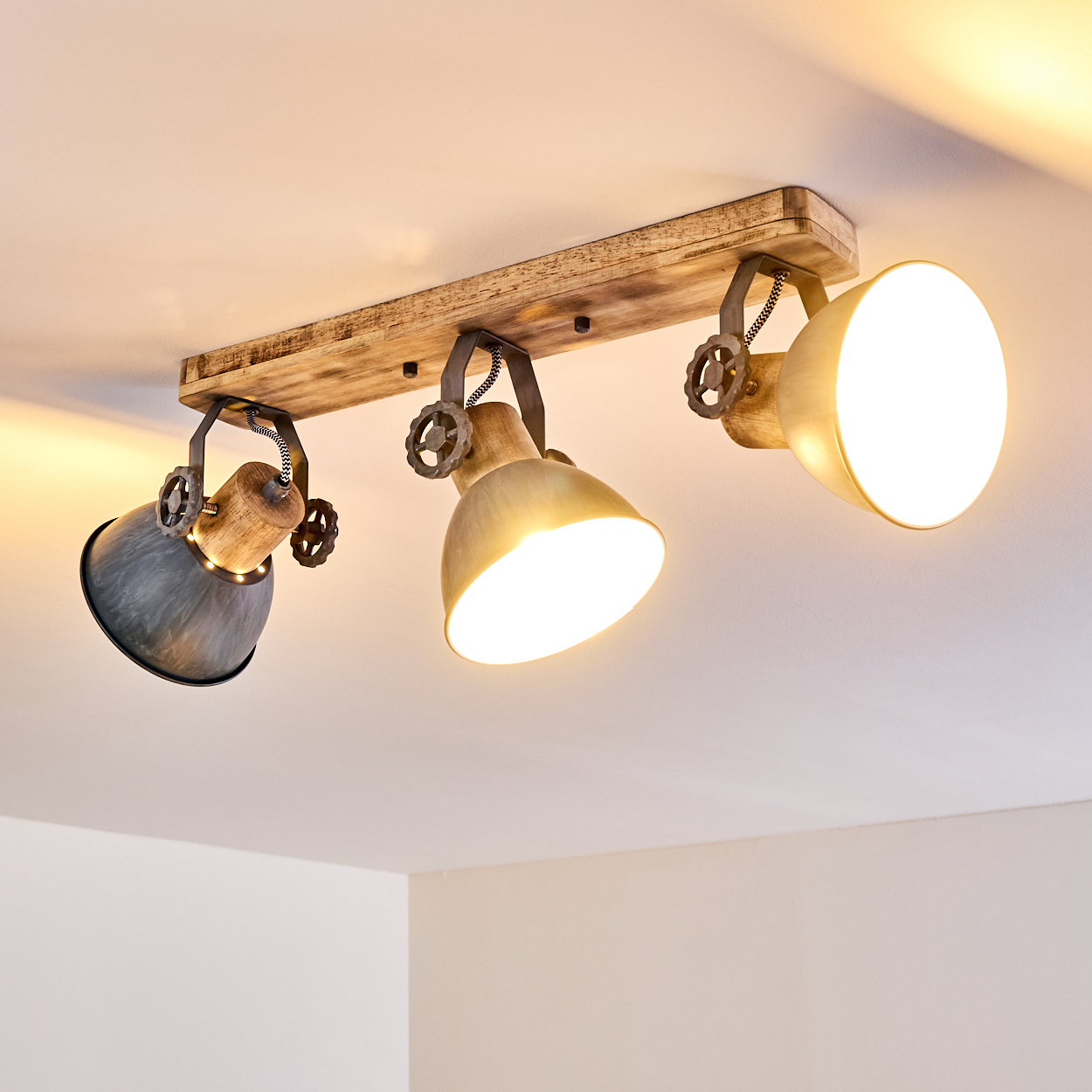 Deckenleuchte mit Holzsockel und drei verstellbaren Lampenschirmen in Grau und Messing.