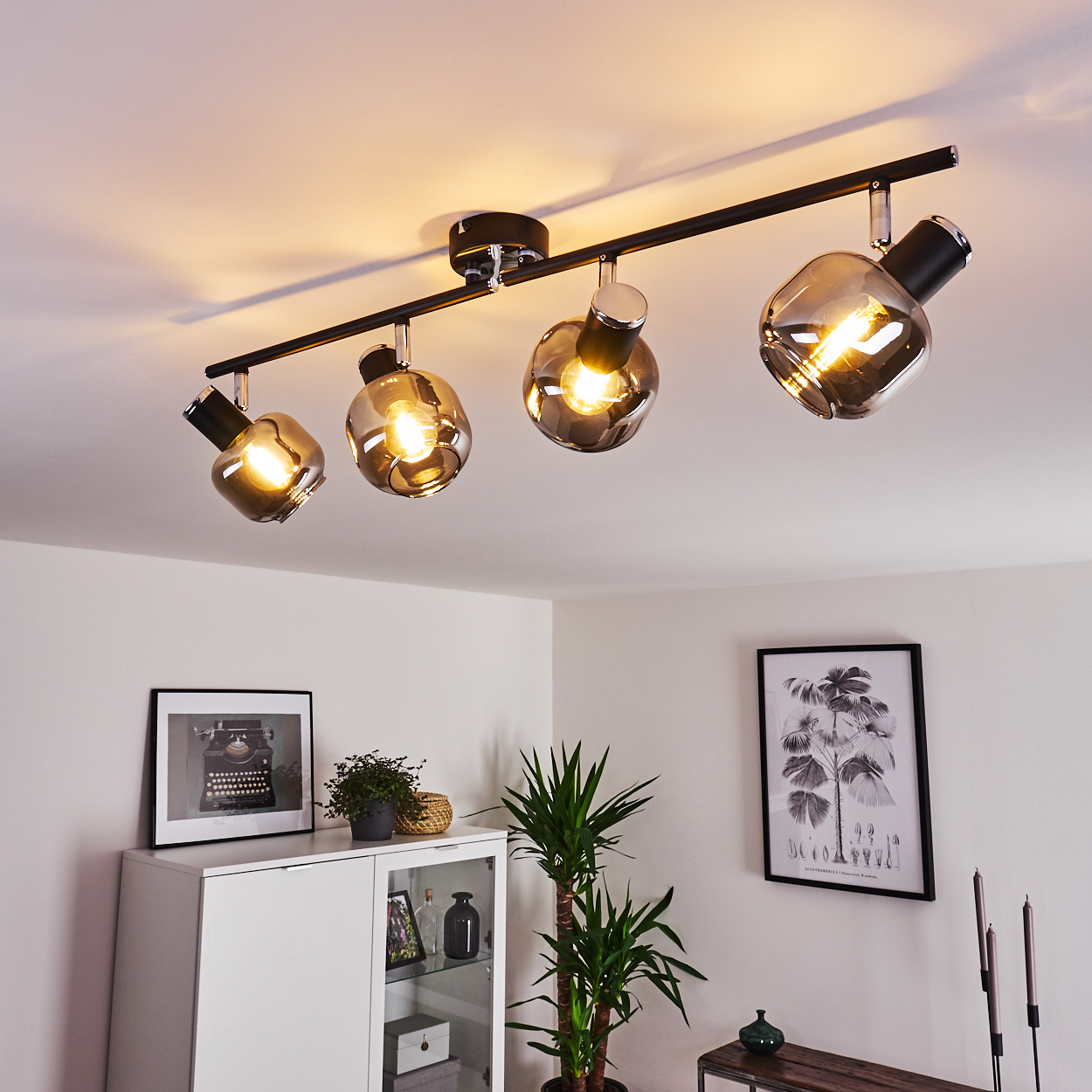 Moderne Deckenleuchte mit vier Rauchglas-Kugeln über einem weißen Schrank mit Bildern.