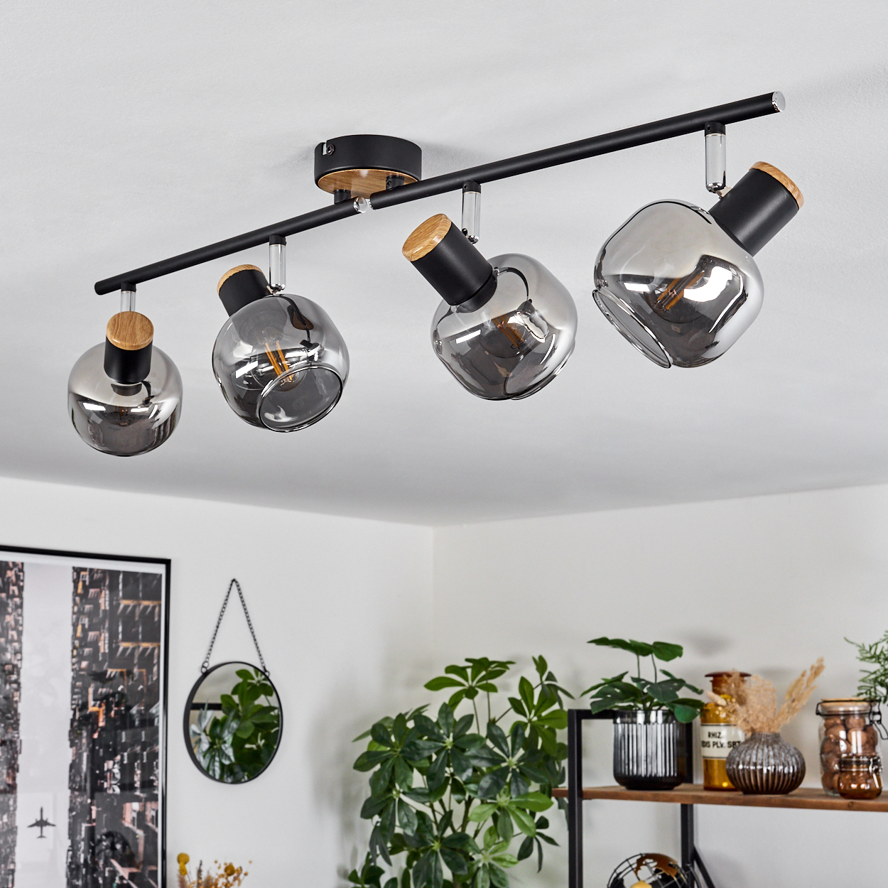 Eine schwarze Schienenleuchte mit vier rauchglasernen Kugeln und Holzakzenten hängt an einer weißen Decke.