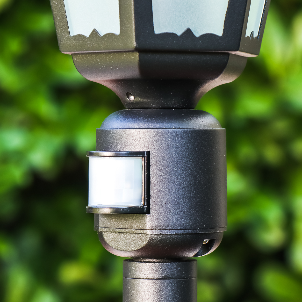 Ein schwarzer Bewegungsmelder an einer Lampe, im Hintergrund grüne Blätter.