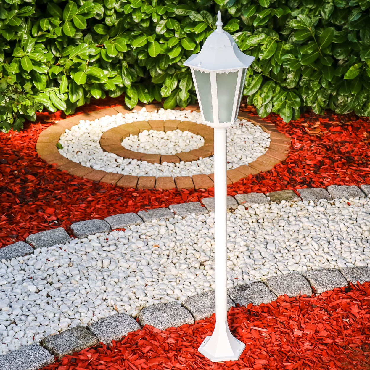Ein weier Laternenpfahl steht in einem Garten mit roten Mulch- und weien Kieselwegen.