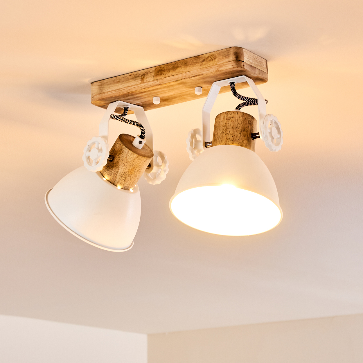 Zwei weiße Lampenschirme hängen an einem Holzbalken mit weißen Halterungen.