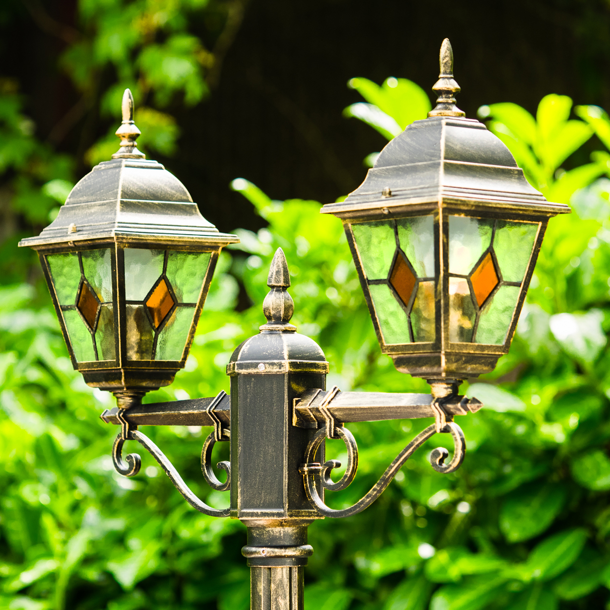 Eine zweilampige Gartenlaterne aus dunklem Metall mit grünem Glas und orangefarbenen Akzenten.