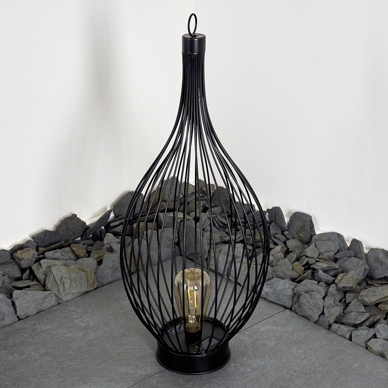 Eine schwarze Drahtlampe mit einer Glühbirne, umgeben von Steinen.